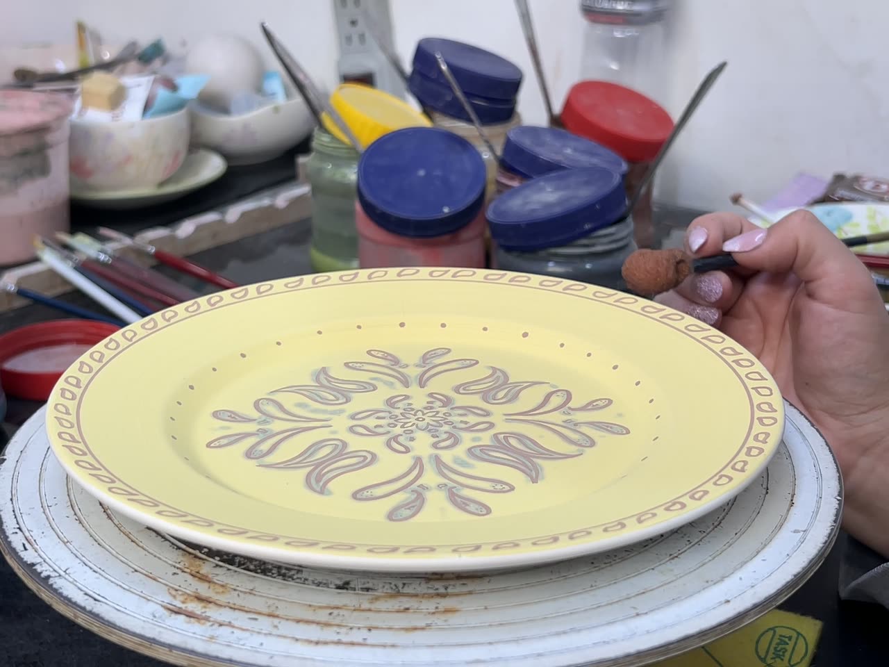 Manos pintando un plato en el taller